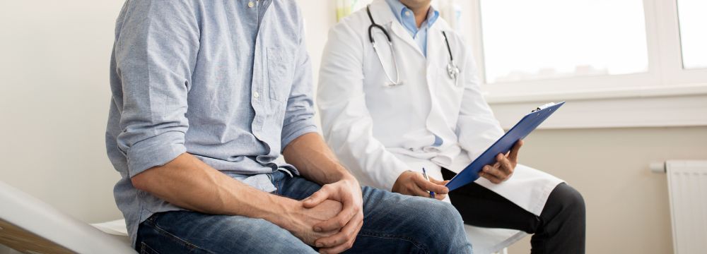 Male patient discussing treatment options with urologist while sitting on medical bed